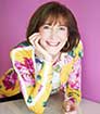 Author LSR wearing bright multi-colored dress and smiling with hand on face